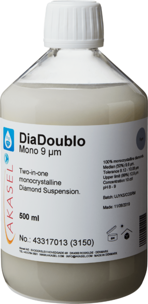 Akasel DiaDoublo Mono 9 µm: A 500 ml plastic bottle with a white screw cap, filled with a light, milky-white monocrystalline diamond suspension. The label shows the product name “DiaDoublo Mono 9 µm” along with the description “Two-in-one monocrystalline Diamond Suspension.” Additional information includes: “100% monocrystalline diamonds,” “Median (50%) 9.6 µm,” “Tolerance 9.12 – 10.08 µm,” “Upper limit (99%) 12.9 µm,” and a concentration of “10 ct/l.” Symbols on the label provide instructions on storage and shelf life.