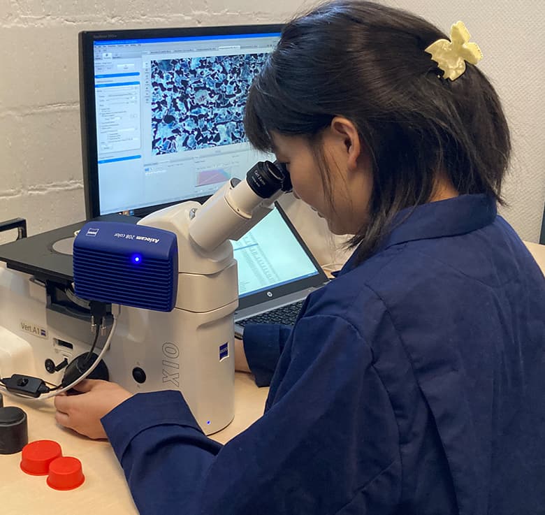 Akasel technician analyzing a sample using a Zeiss Axio microscope after metallographic sample preparation, with the microscopic image displayed on the computer screen.