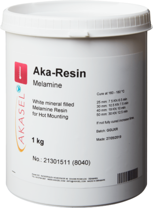 Akasel Aka-Resin Melamine: White plastic container filled with white, mineral-filled melamine resin for hot mounting. The label includes the Akasel logo and product details: "Aka-Resin Melamine," "White mineral-filled Melamine Resin for Hot Mounting," "1 kg." Technical details specify curing conditions: "Cure at 160 – 180 °C," diameter and force values (e.g., 25 mm: 10 kN, 4–5 min/2–3 min), and instructions to extend curing time if incomplete. The label also features a batch number, manufacturing date, and hazard warnings. Specifically designed for metallographic applications, ideal for embedding white samples for precise and stable analysis.